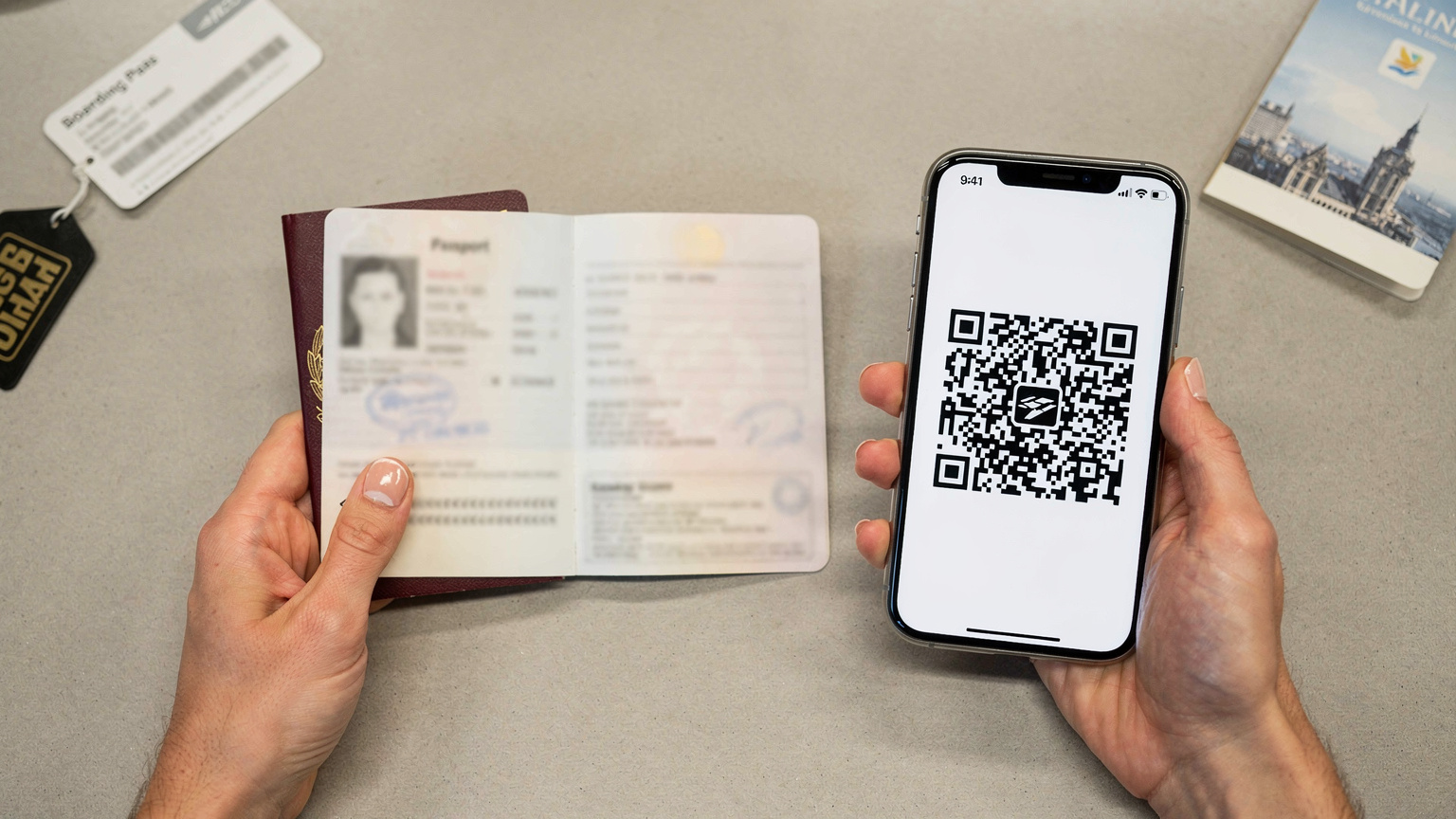 Due mani tengono un passaporto italiano aperto e uno smartphone che mostra un codice QR, in un contesto che suggerisce il check-in in un aeroporto o in un hotel, con dettagli di viaggio sfocati sullo sfondo.