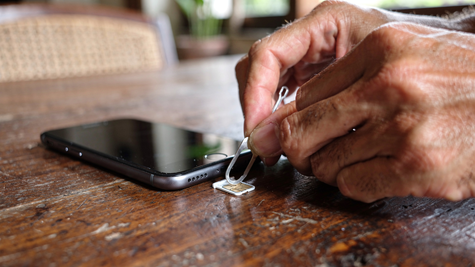 Manos de un viajero deslizando una tarjeta SIM física fuera de su bandeja de teléfono, un gesto que la eSIM elimina por completo.